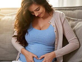 Síntomas horas antes del parto que debes saber Mujer embarazada acariciando su vientre, sonriendo y sentada en un sofá.