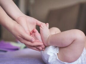Cómo tratar las rozaduras de bebé en casa Mamá sosteniendo los pies de su bebé recién nacido en pañal.